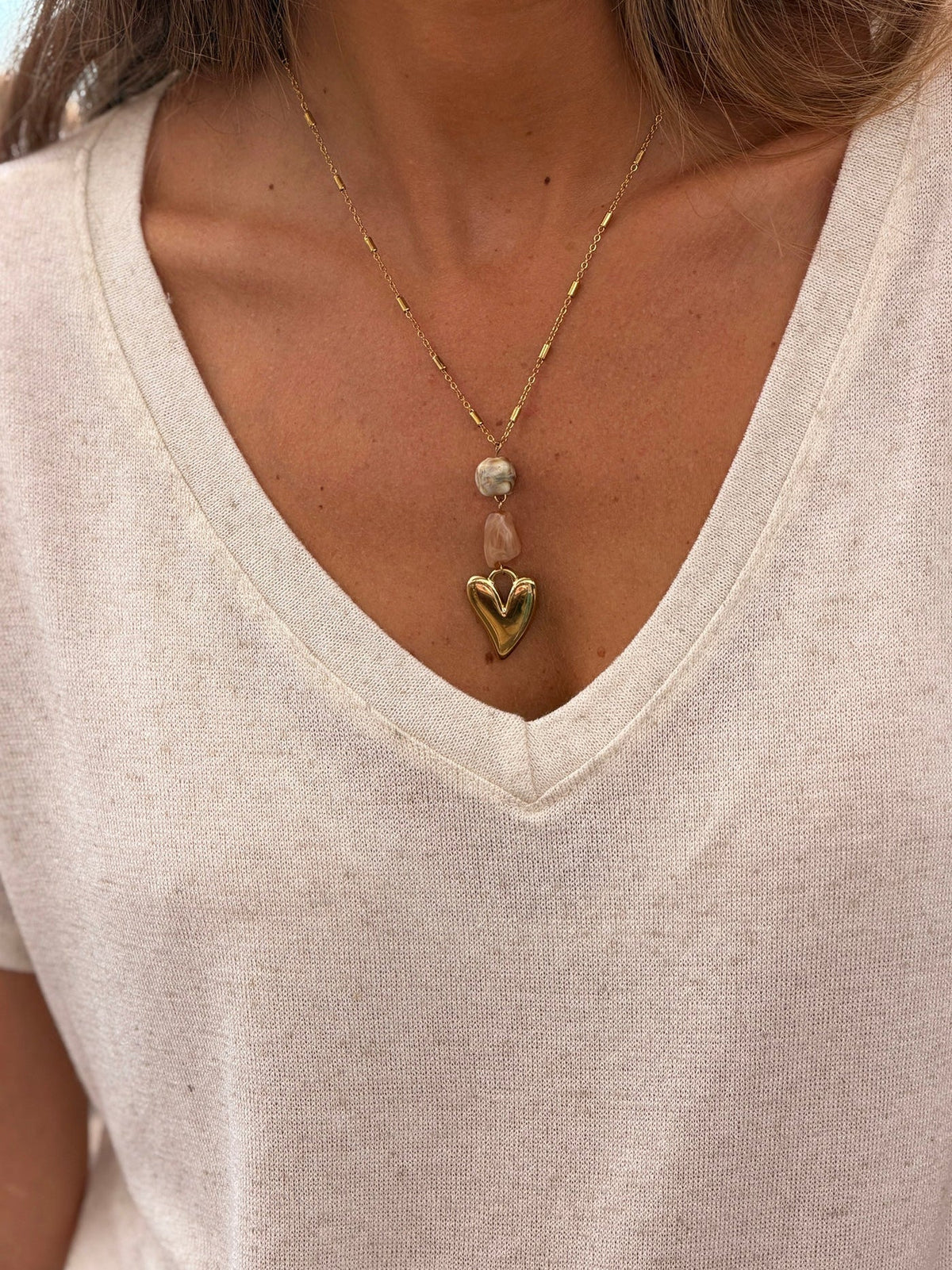 ELEGA — Accessoires : collier chaîne dorée à pendentif cœur porté sur un haut crème