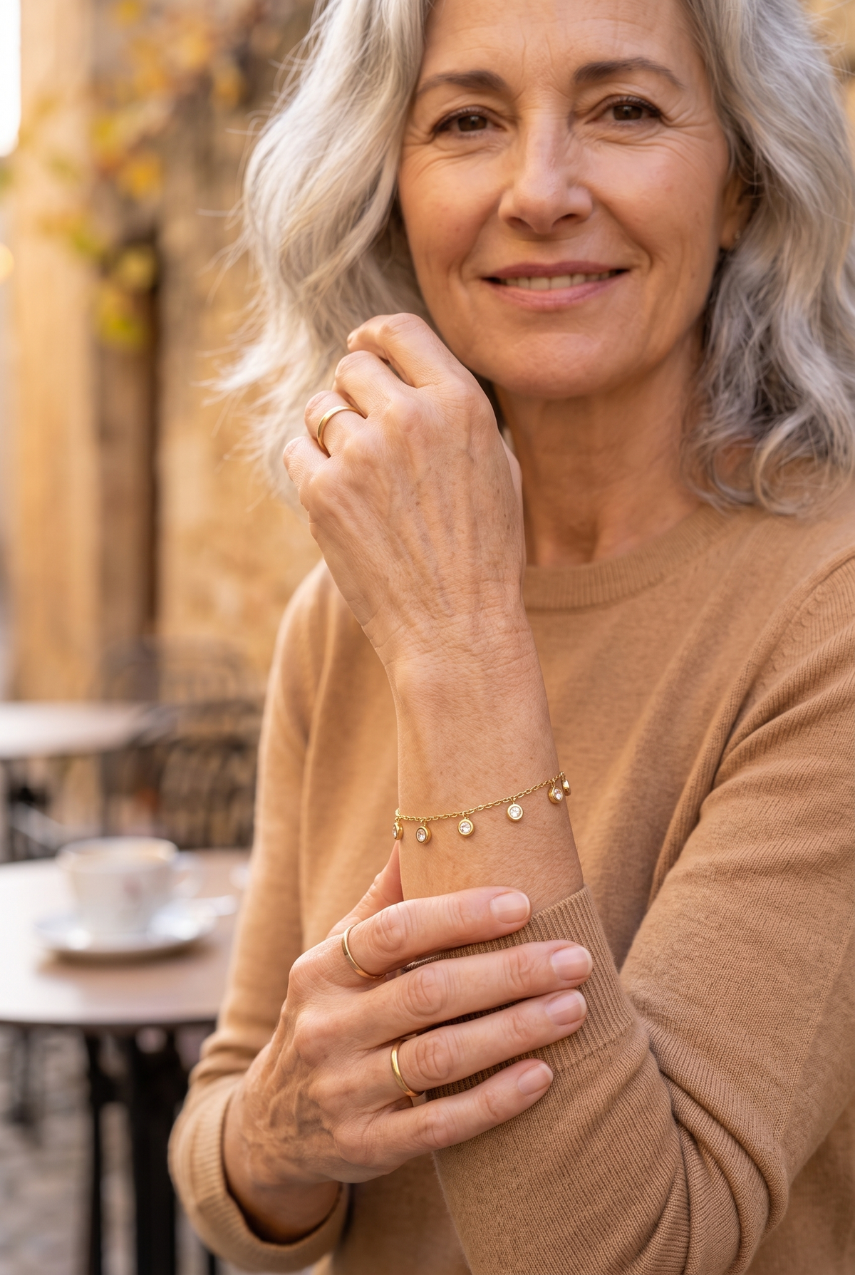 ÉLISE — pulsera de cadena fina dorada con colgantes de pedrería, en una terraza en otoño