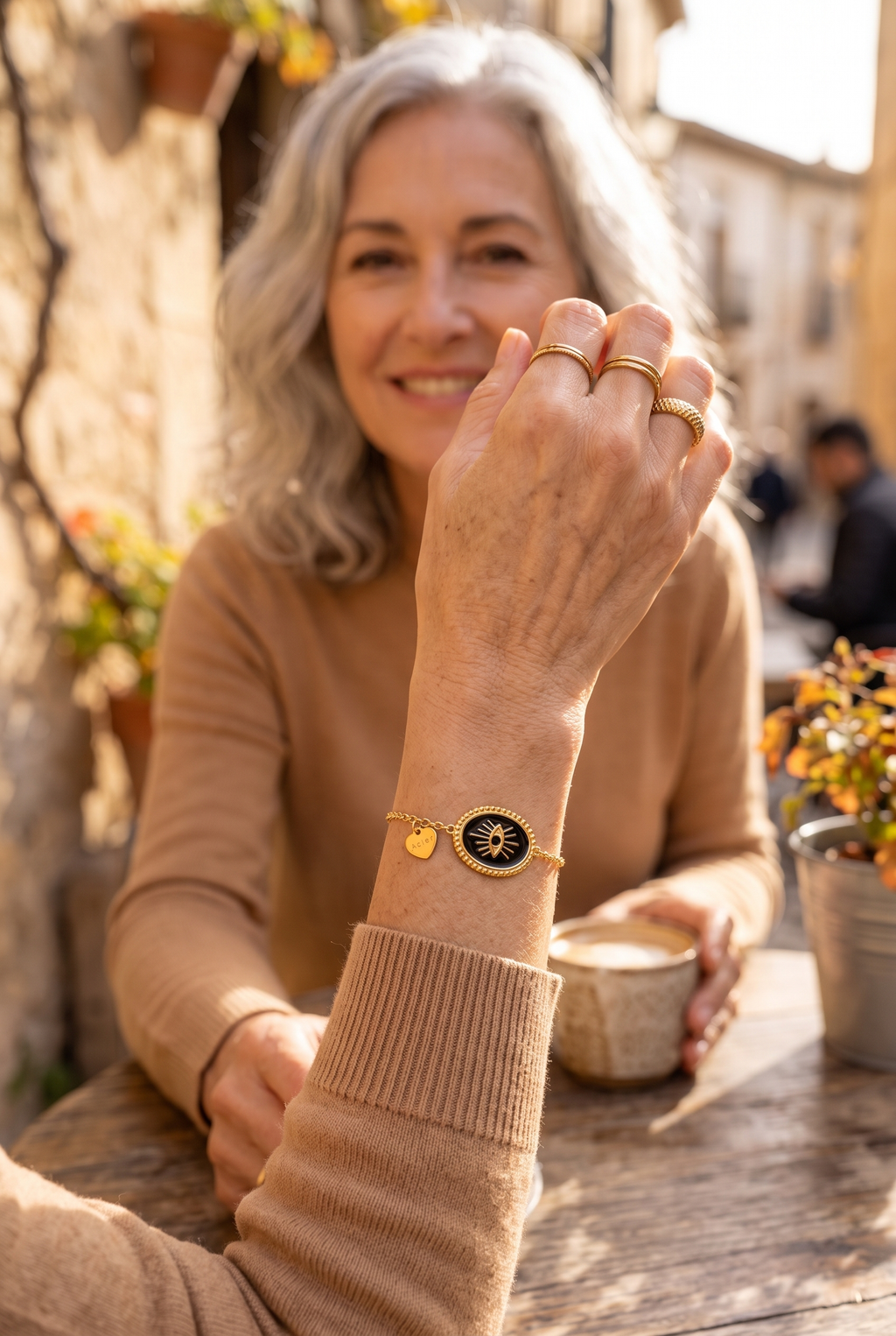 CORALIE — pulsera de eslabones finos dorados con ojo negro, en una terraza en otoño