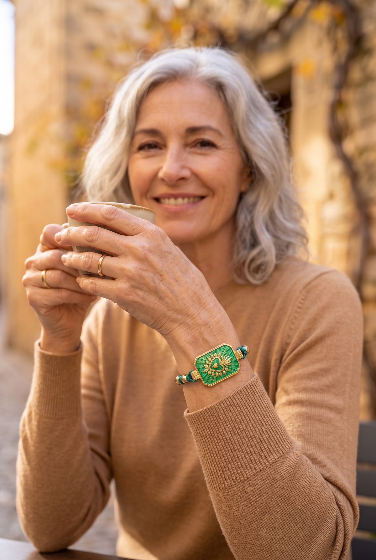 CLÉMENCE — pulsera de cordón brillante con placa verde y corazón dorado, en una terraza en otoño