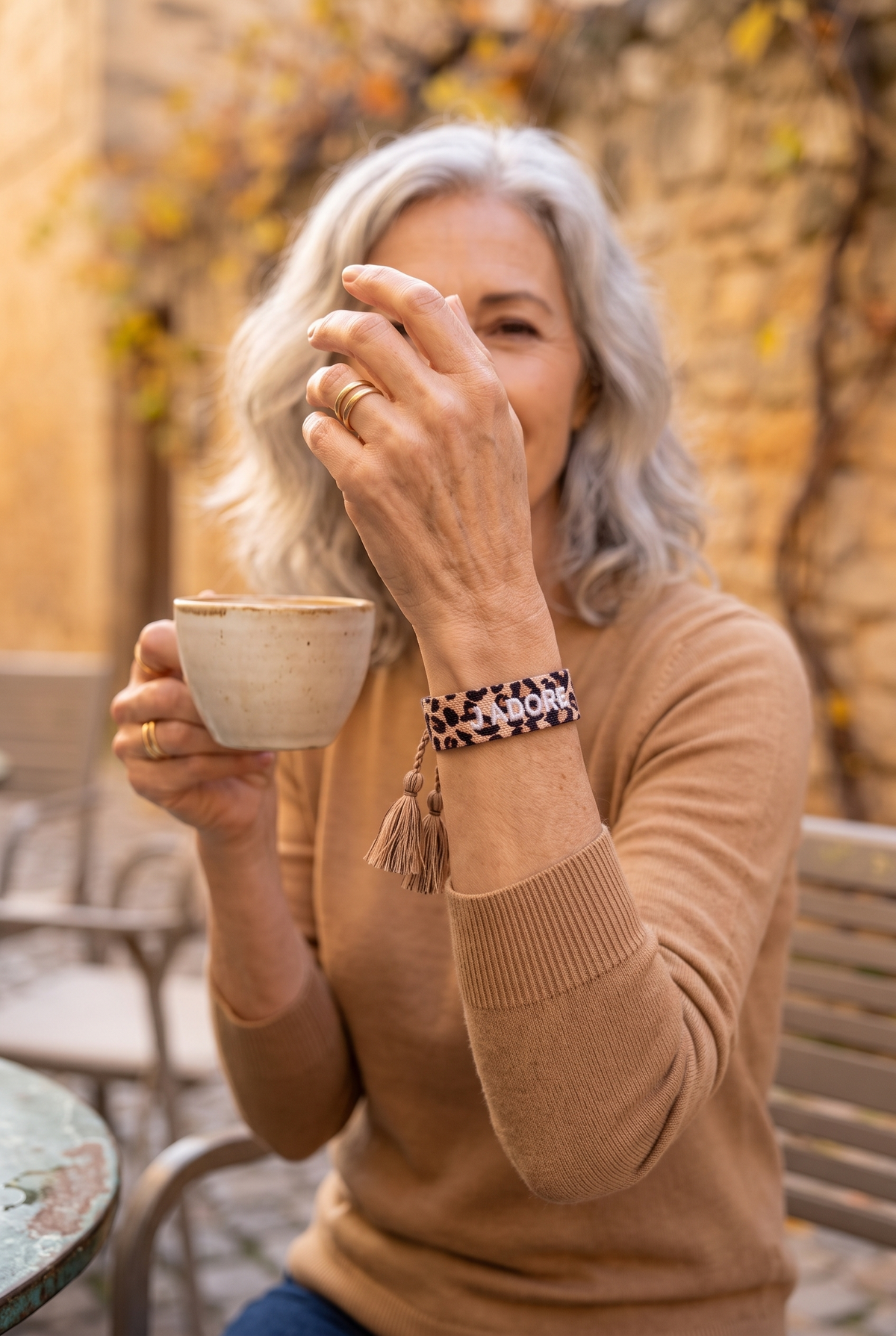 CLARISSE — pulsera de tela con estampado de leopardo ajustable con pompones y bordado J'adore blanco, en una terraza en otoño